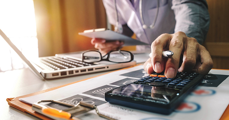 Hands of doctor with calculator and laptop