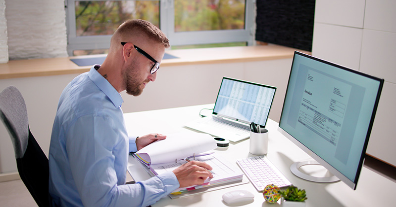 Man at desk reviews invoice document in front of compute