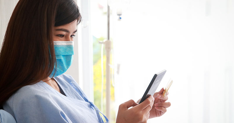 Patient wearing mask and using phone to pay medical bill