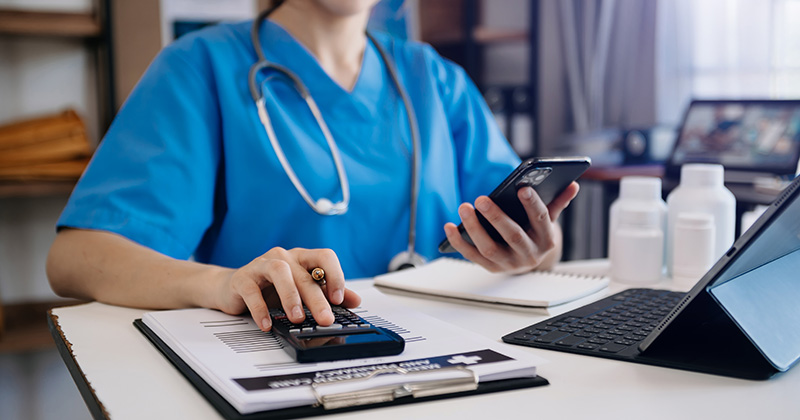 PERSON IN SCRUBS LOOKING AT PHONE WITH CALCULATOR