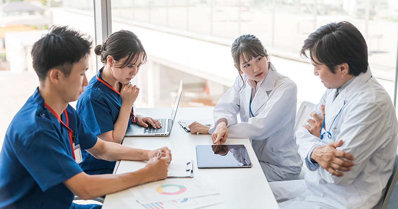 TWO DOCTORS AND TWO NURSES SITTING AT TABLE